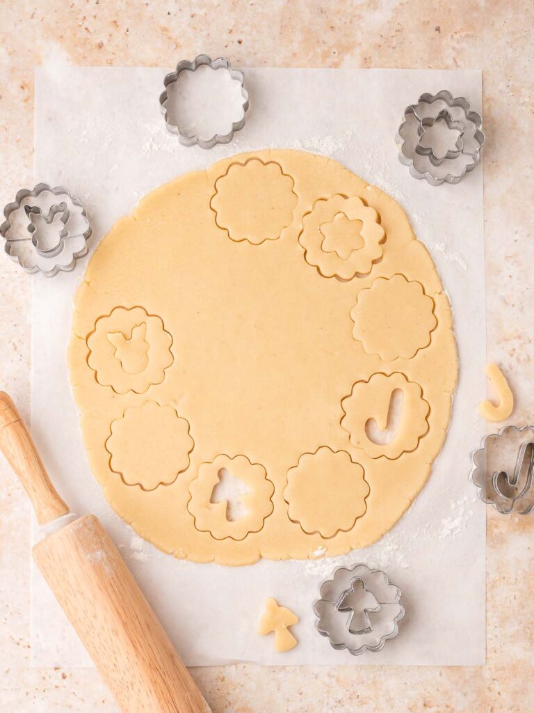 Dough being cut into scalloped rounds and festive cut-out centers with cookie cutters.