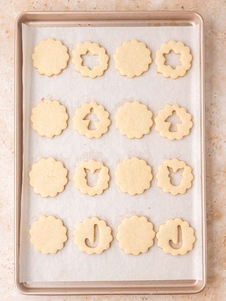 Freshly baked Linzer cookie tops and bottoms cooling on a parchment-lined baking sheet.