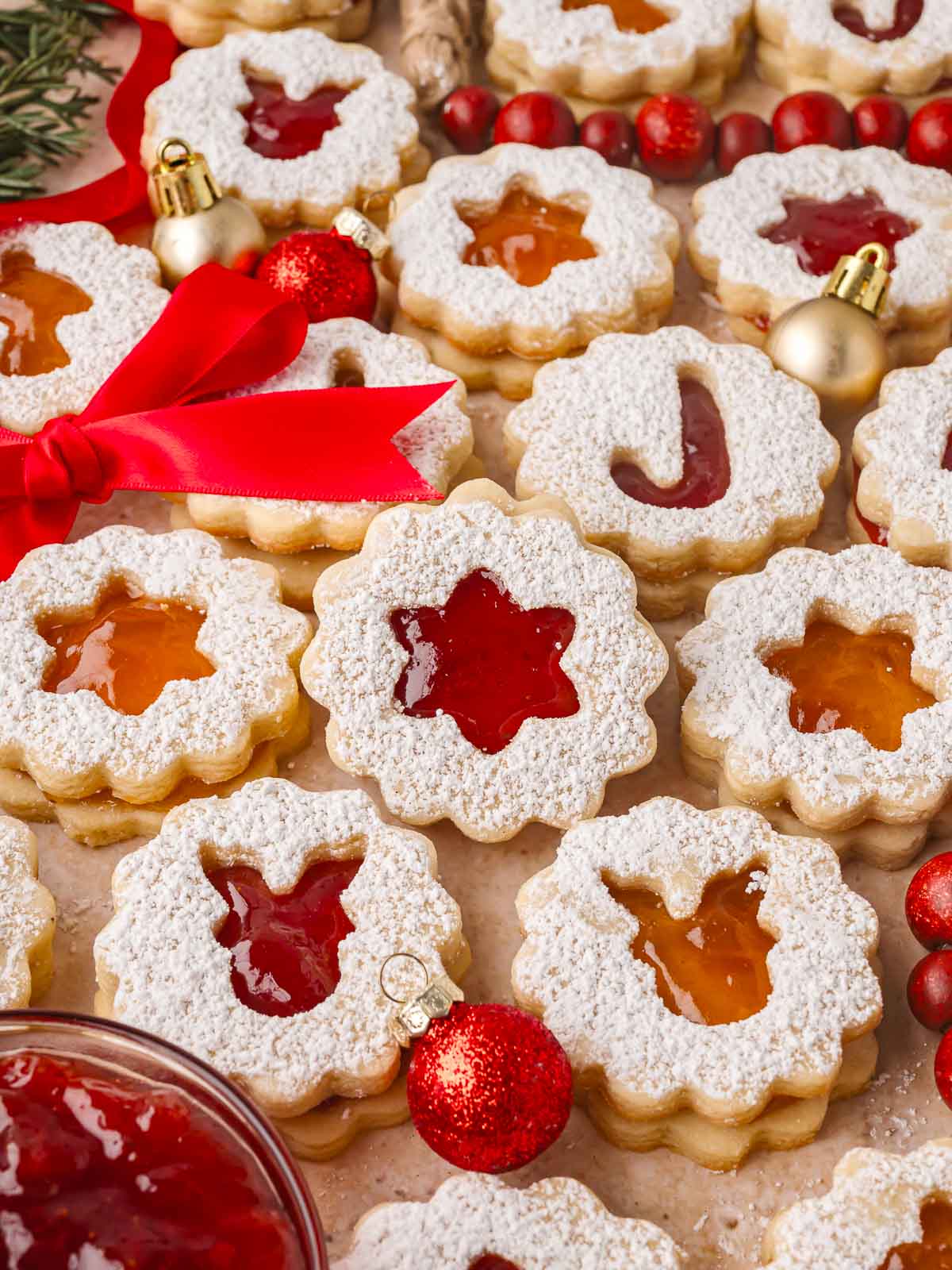 Soft almond cookie dusted with powdered sugar and filled with glossy red jam, perfect for holiday baking.