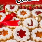 Linzer cookies with jam filling and powdered sugar ona serving dish with christmas decorations all around them.