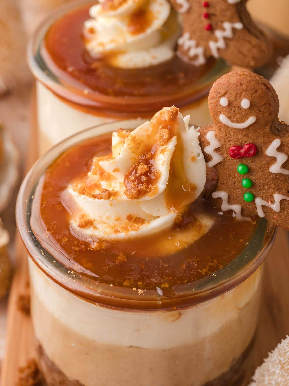 Close-up of Mini Gingerbread Trifles topped with whipped cream, caramel drizzle, crushed cookies, and decorated with small gingerbread man cookies.