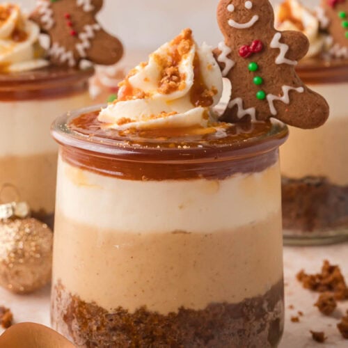 Mini Gingerbread Trifle in a glass jar with layers of gingerbread cake, spiced cheesecake filling, whipped cream, caramel, and a mini gingerbread man cookie on top.
