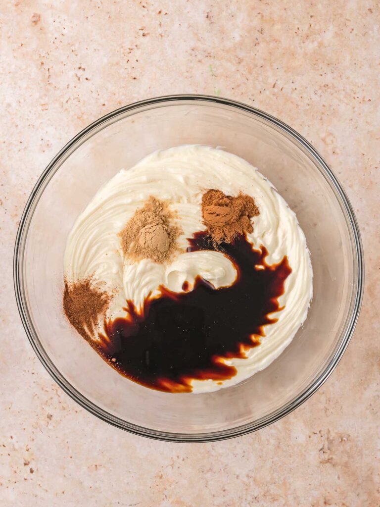 Cream cheese mixture in a glass bowl with molasses, cinnamon, ginger, and nutmeg added on top for the spiced cheesecake filling for Mini Gingerbread Trifle.