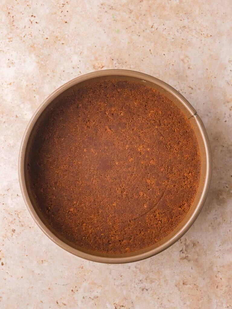 Gingersnap crust pressed into the bottom of a springform pan for no bake gingerbread cheesecake.
