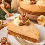 Slice of creamy No Bake Gingerbread Cheesecake on a white plate with whipped cream and a mini gingerbread cookie on top.