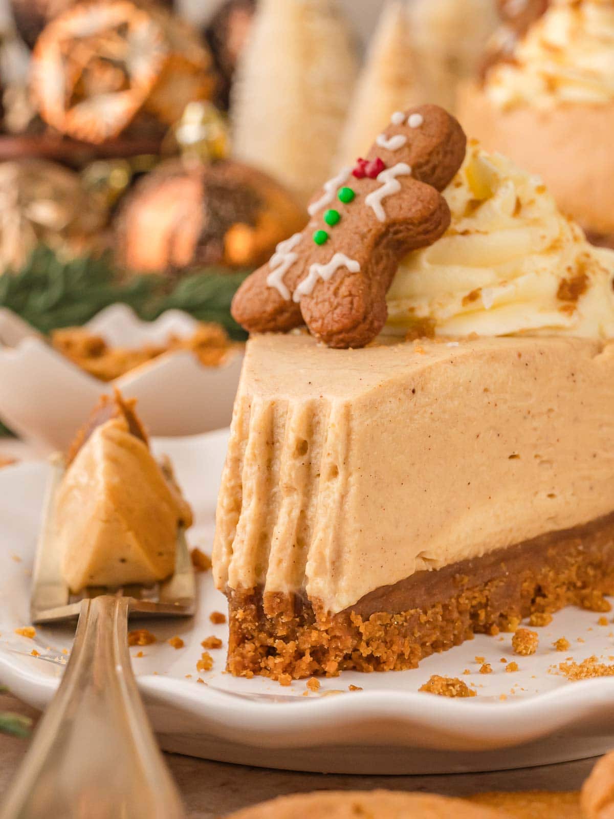 No Bake Gingerbread Cheesecake slice on fork showing creamy texture and thick gingersnap base, topped with a decorated gingerbread man.
