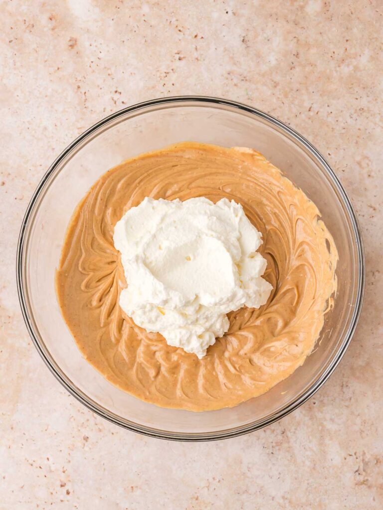 Creamy gingerbread cheesecake mixture in bowl with whipped cream ready to be mixed in.
