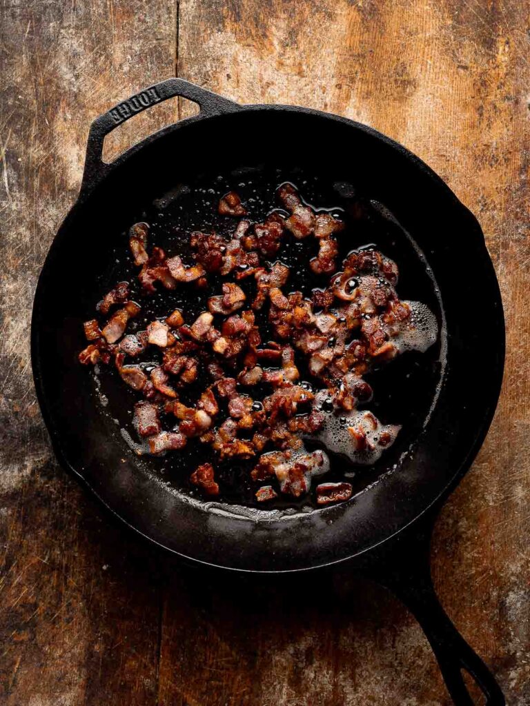 Crispy bacon cooking in a cast iron skillet for cheesy green beans.
