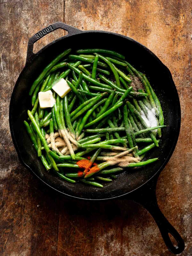 Green beans in skillet with butter and seasonings for cheesy green beans.