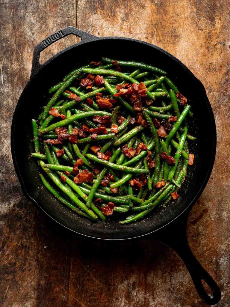 Green beans tossed with crispy bacon in skillet before adding cheese.