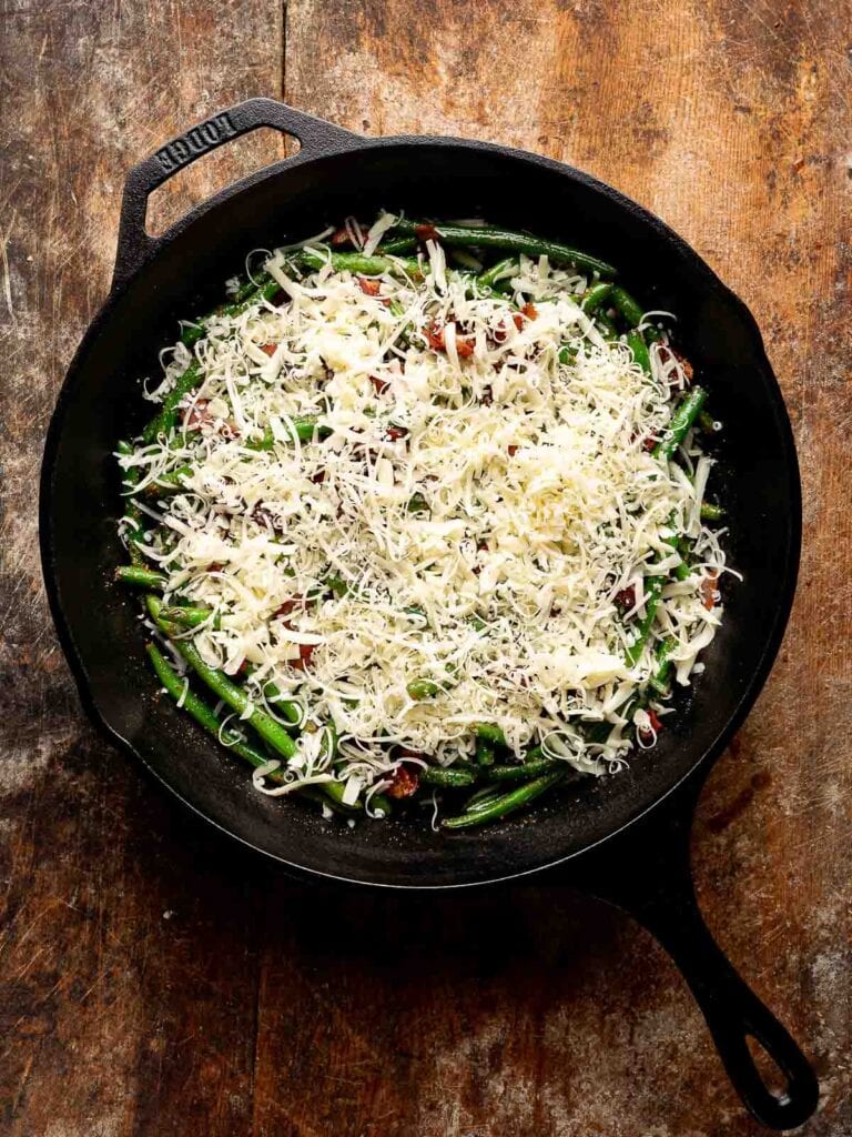 Shredded mozzarella and Parmesan layered over green beans and bacon in skillet.