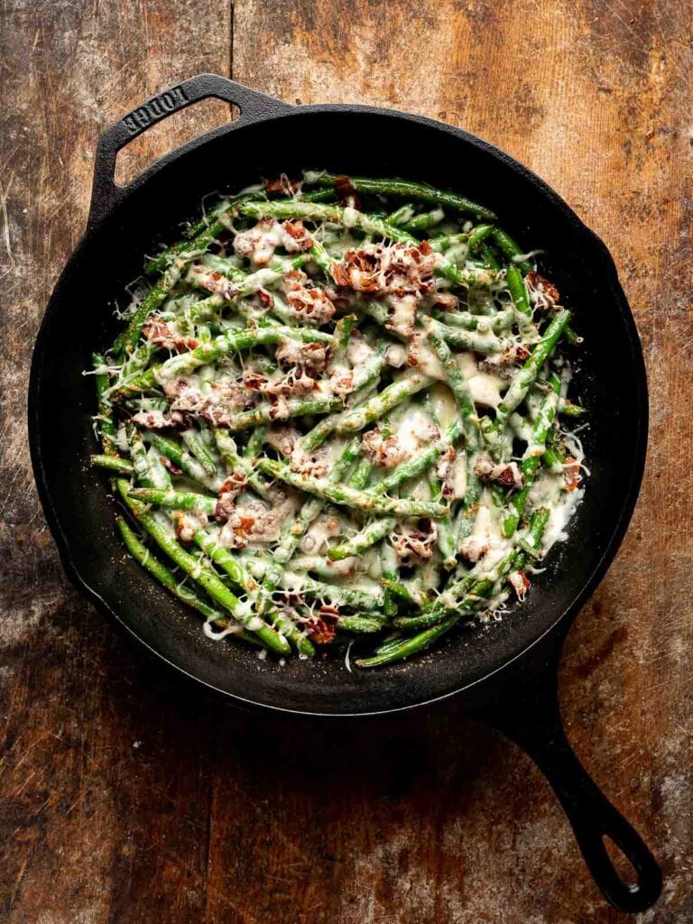 Cheesy green beans with garlic and bacon bubbling in skillet after cooking.