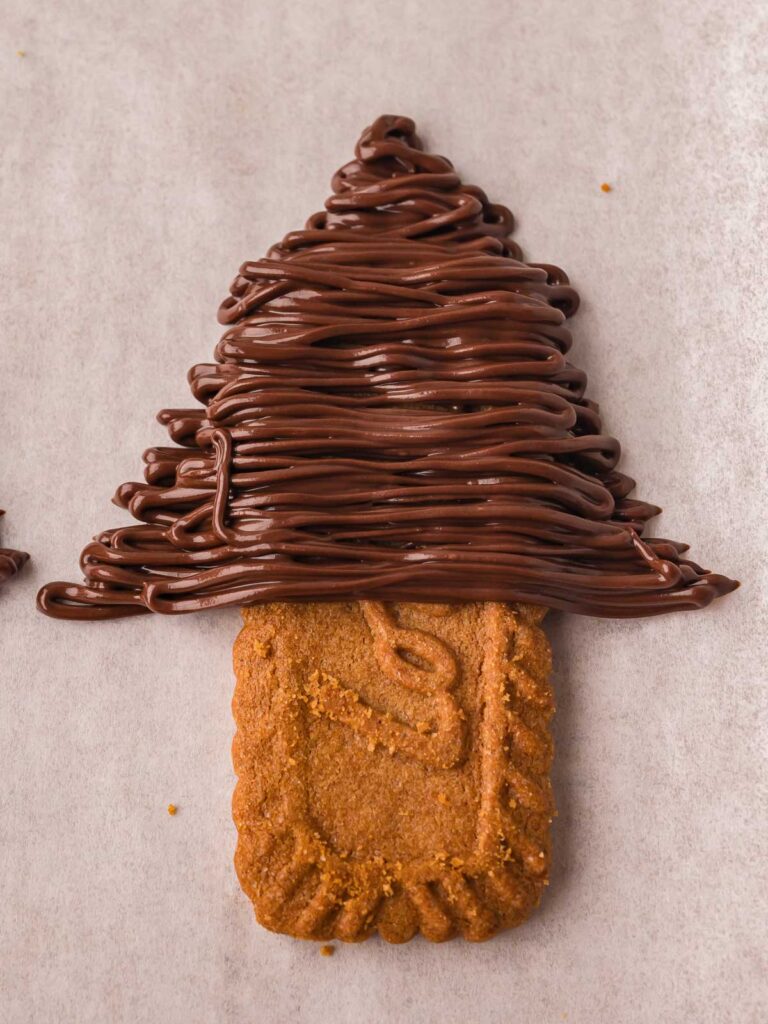 Pipped melted chocolate in zigzag lines to form Christmas tree shapes above each cookie.