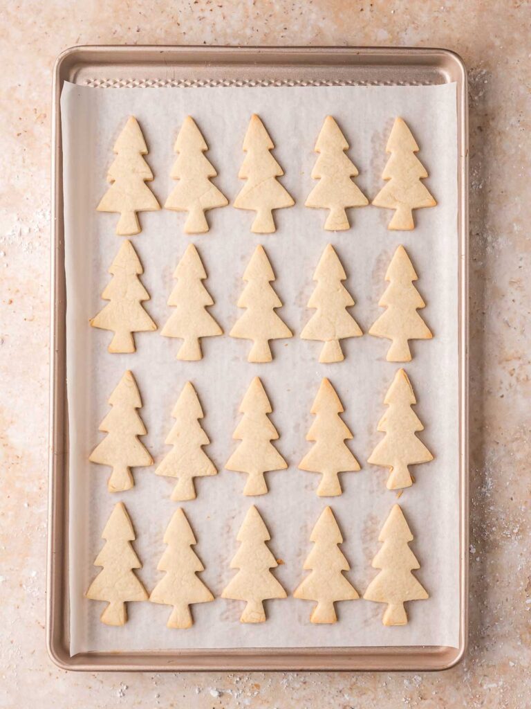 Freshly baked Christmas tree cut-out sugar cookies cooling on a parchment-lined baking sheet.