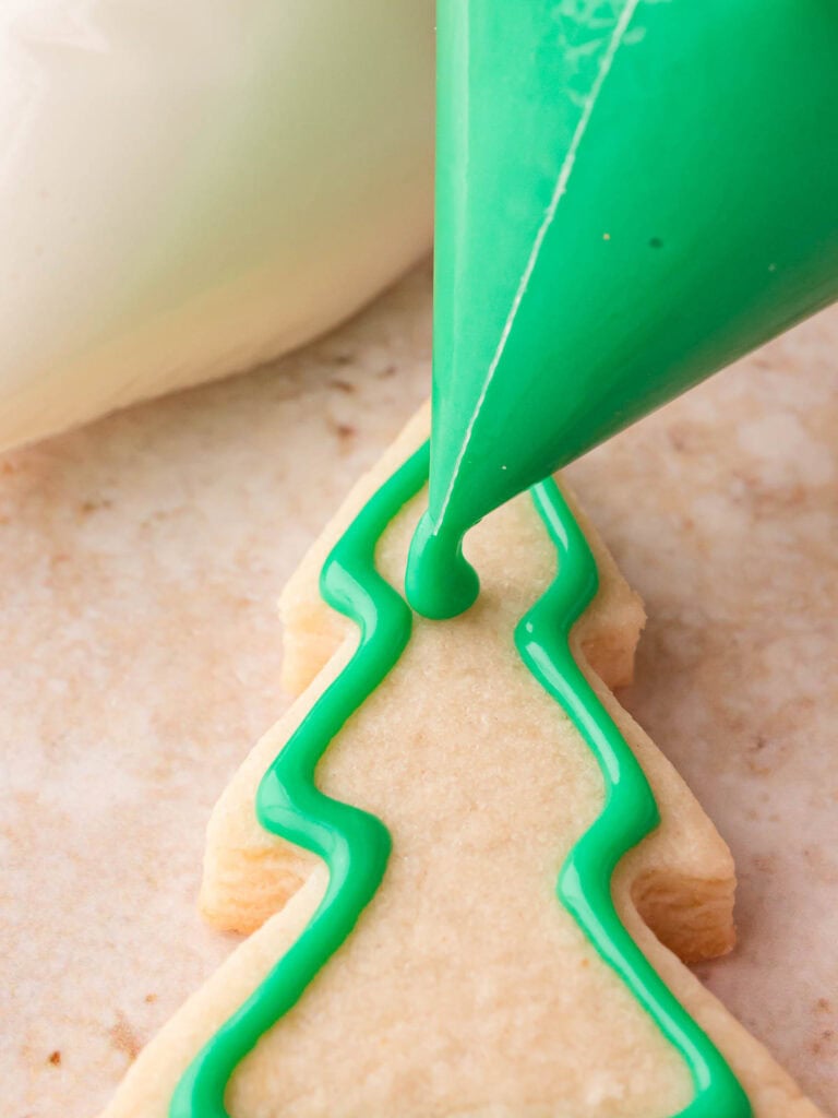 Piping green glaze around the edge of a Christmas tree sugar cookie for decorating.