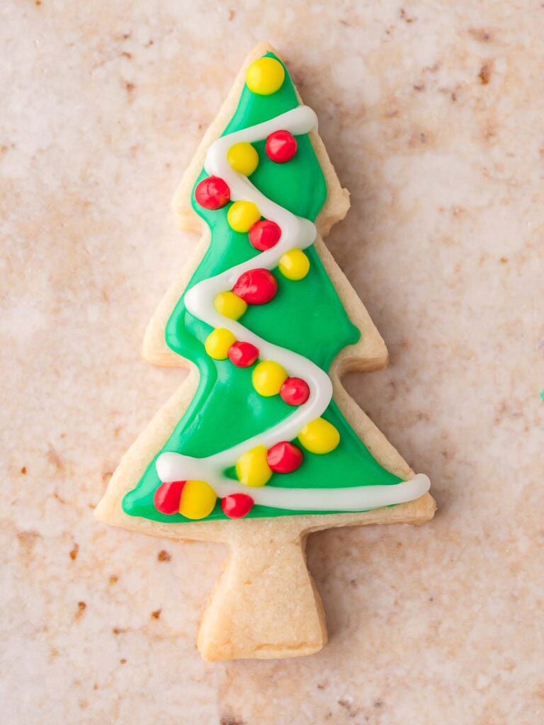 Finished decorated Christmas tree sugar cookie with green icing, white garland, and red and yellow candy ornaments.