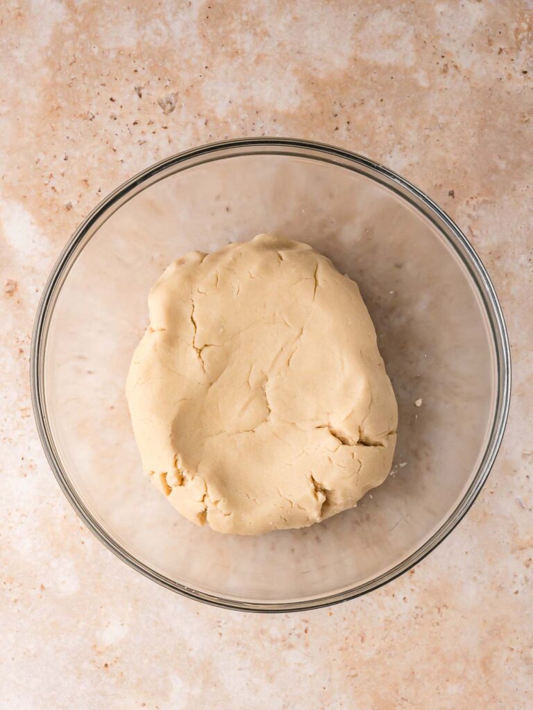 Smooth sugar cookie dough formed into a ball in a glass bowl before chilling.