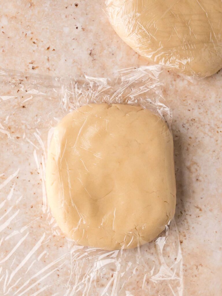 Sugar cookie dough divided into discs and wrapped in plastic wrap before chilling.
