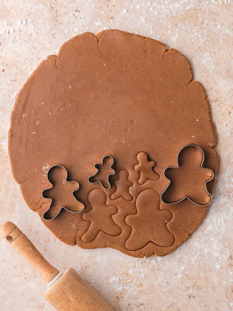 Rolled-out gingerbread dough with cookie cutters making gingerbread man shapes.