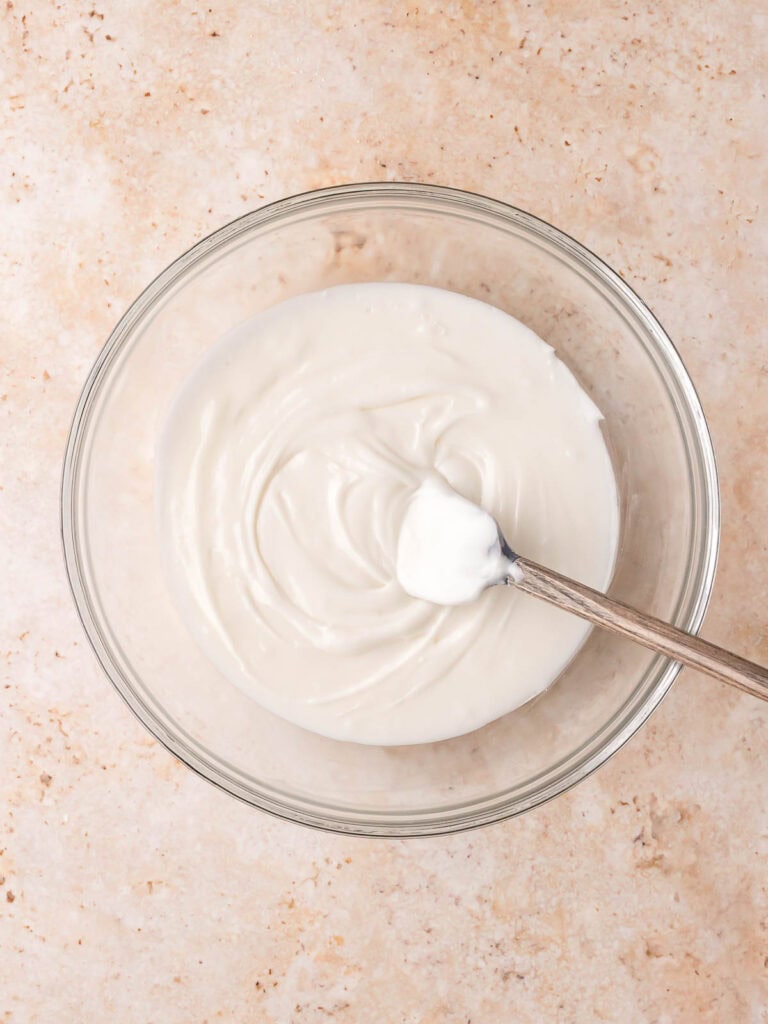 Bowl of white icing for decorating Gingerbread Man Cookies with a spoon inside.