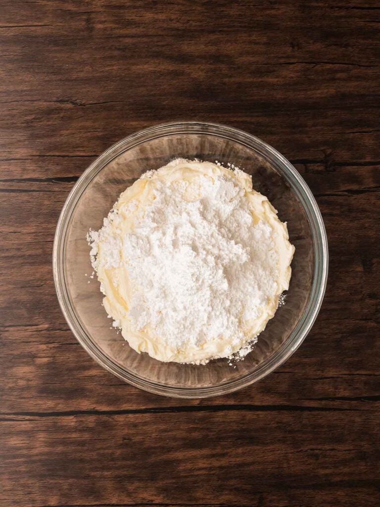 Butter and cream cheese mixture topped with powdered sugar for the base of no-bake Coconut Snowball Cookies.