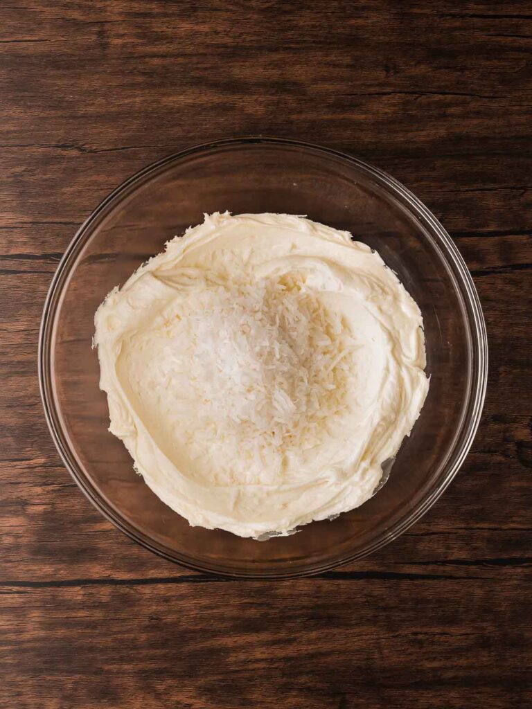 Shredded coconut being mixed into the creamy cookie mixture to form the Coconut Snowball Cookie dough.