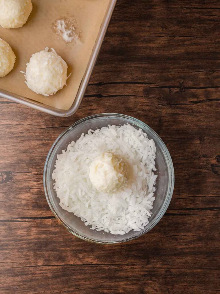 Coconut Snowball Cookie being rolled in shredded coconut for a snowy white coating before chilling.