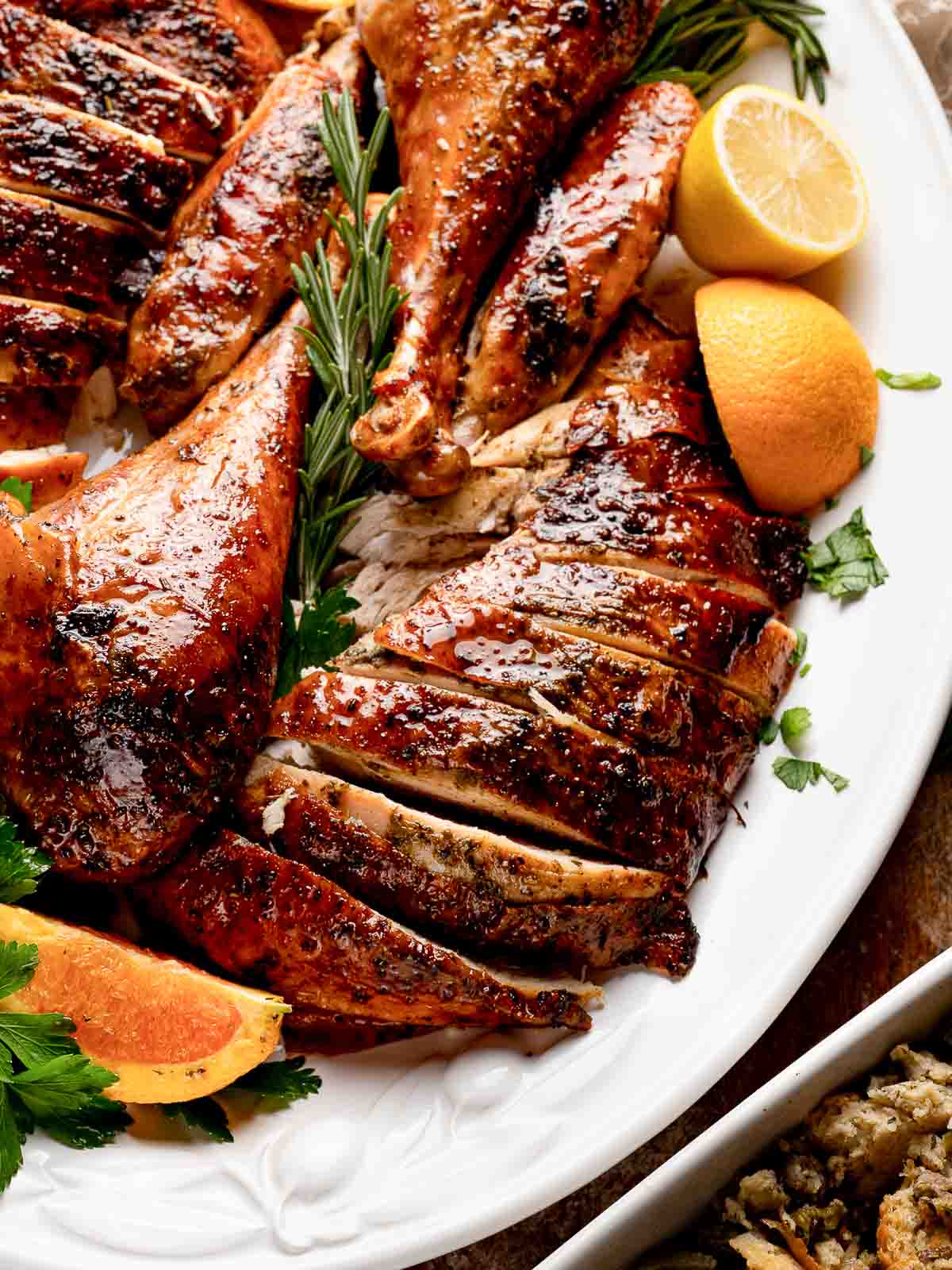 Close-up of juicy sliced turkey breast and legs with citrus wedges and rosemary on a platter ready to serve.