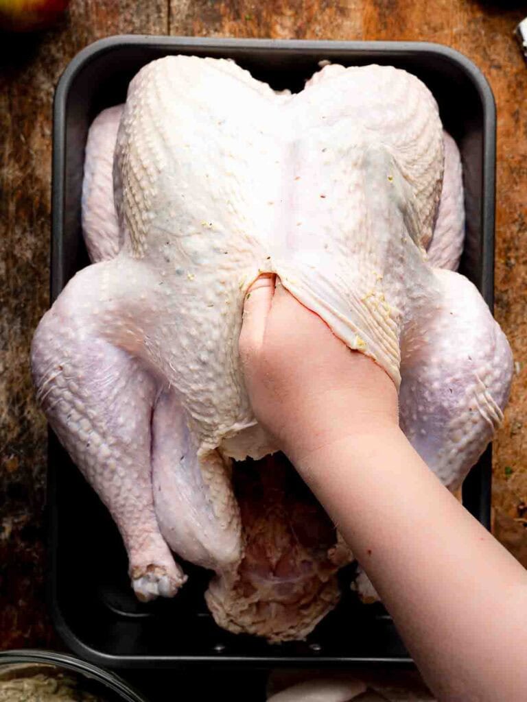 Loosening the skin of a whole turkey to spread herb butter underneath before roasting.