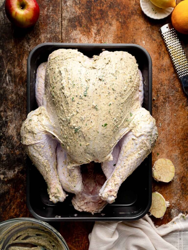 Turkey covered with herb butter mixture and ready for roasting in a pan.