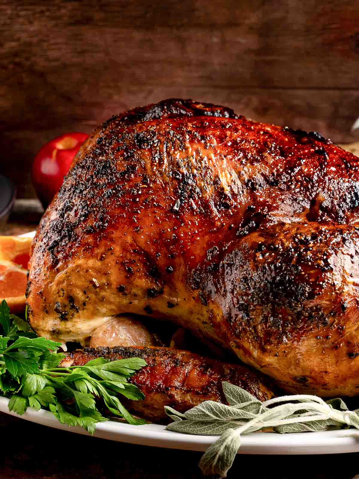 Close-up of golden brown roasted turkey with crispy skin and fresh herbs on serving platter.