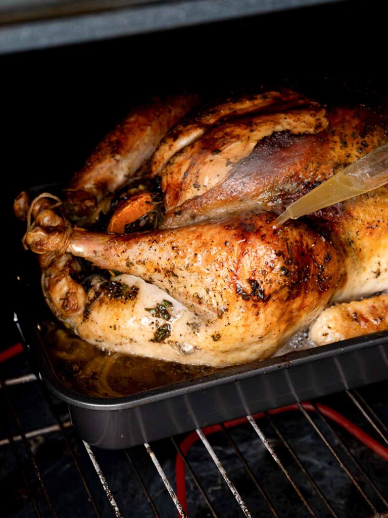 Golden roast turkey basting in the oven with pan juices for a juicy finish.
