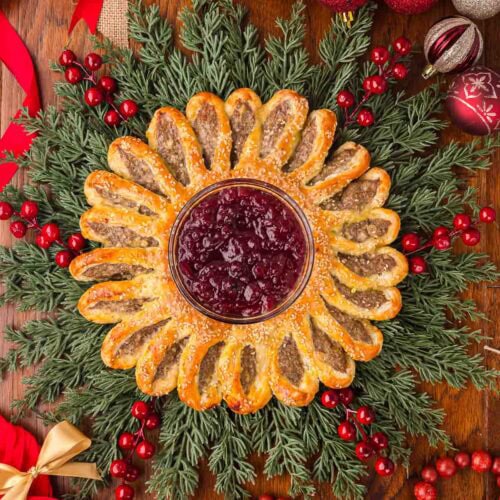 Top view of sausage roll wreath centerpiece with cranberry sauce in the middle and Christmas decorations all around.