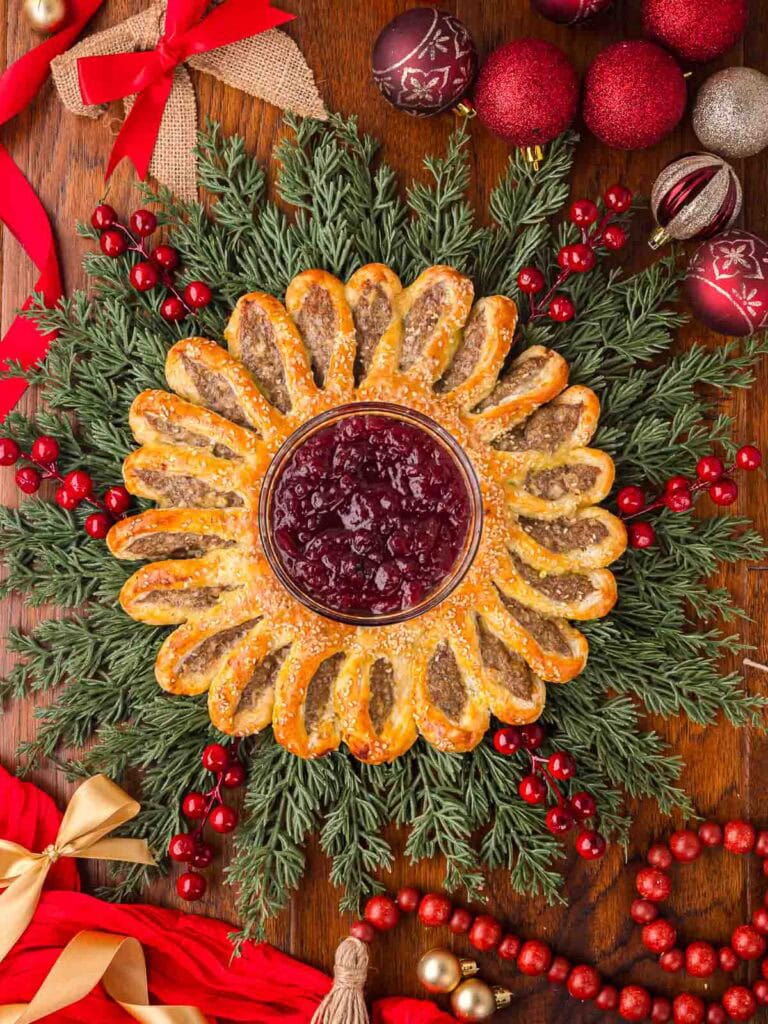 Top view of sausage roll wreath centerpiece with cranberry sauce in the middle and Christmas decorations all around.