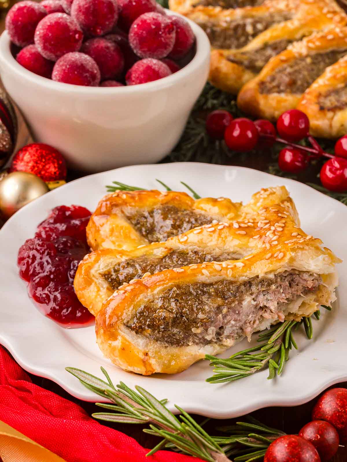 Plate with sliced sausage roll wreath and cranberry sauce garnished with fresh rosemary and sugared cranberries.