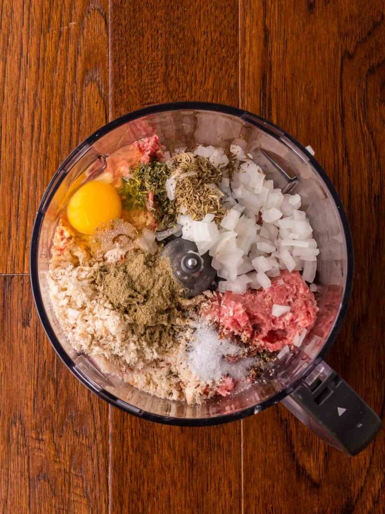 Food processor filled with sausage meat, breadcrumbs, onion, herbs, spices, and an egg for the sausage roll wreath filling.