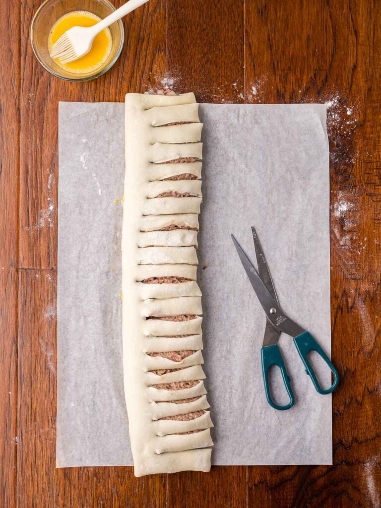 Sausage roll pastry log cut into sections with scissors before forming into a wreath.
