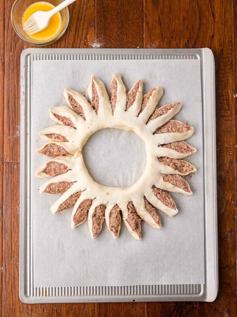 Sausage roll wreath shaped into a circle on a parchment-lined baking tray before baking.