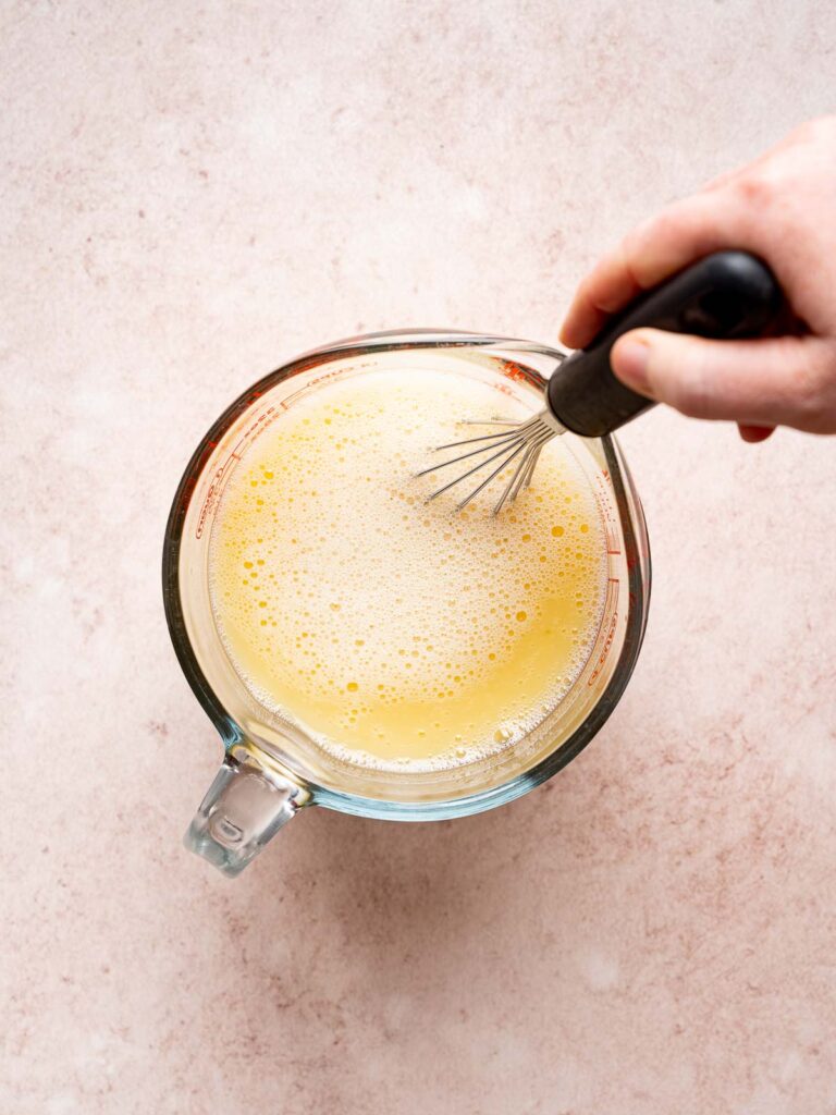 Whisking eggs and chicken broth together in a measuring cup for sourdough stuffing.