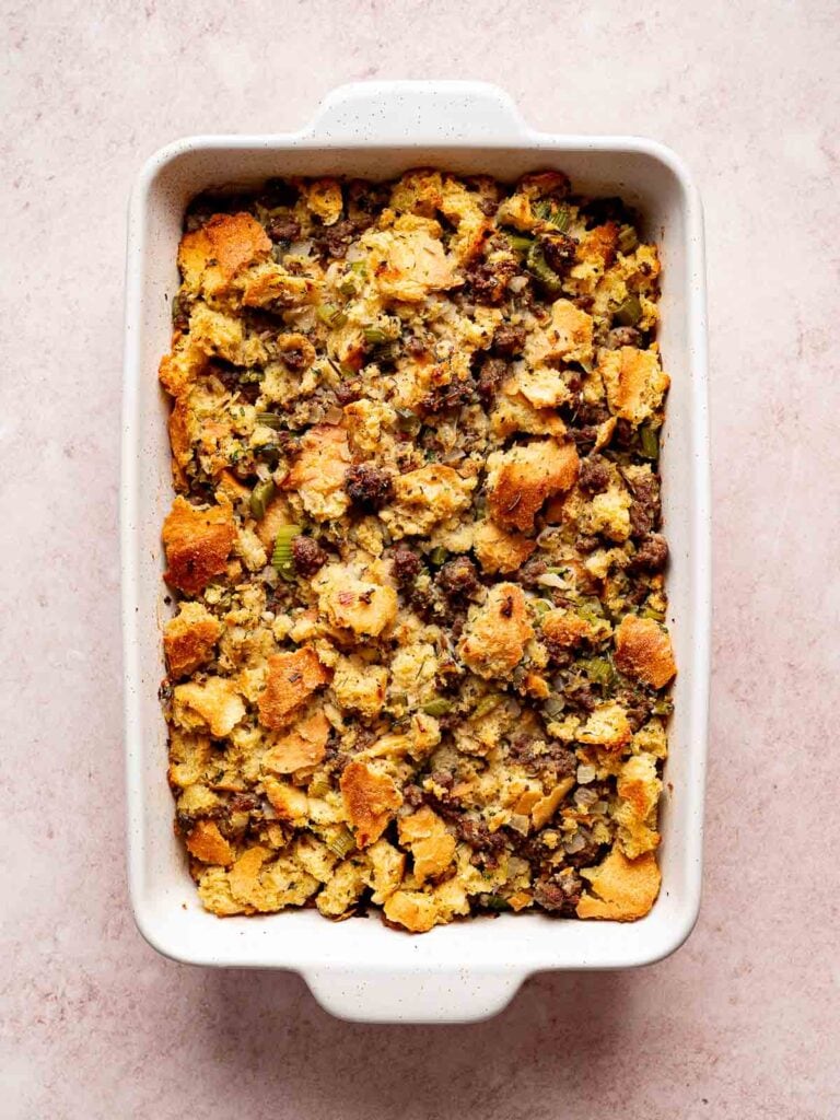 Baked sourdough stuffing with sausage and herbs in a white casserole dish with golden crust.