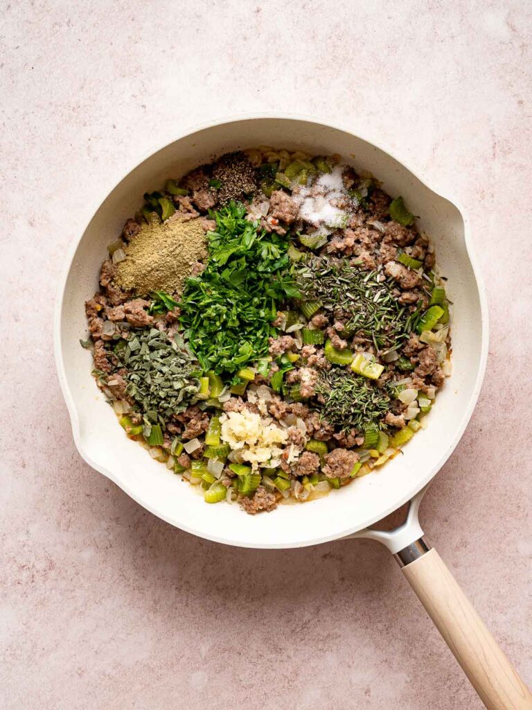 Sausage mixture in a skillet with fresh herbs, garlic, and seasoning for stuffing.