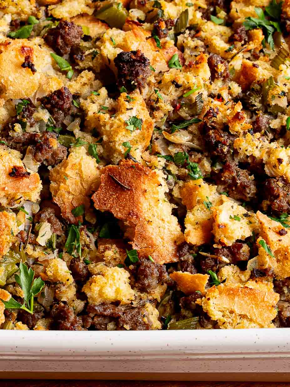 Close-up of baked sourdough stuffing in a white casserole dish topped with toasted bread and herbs.