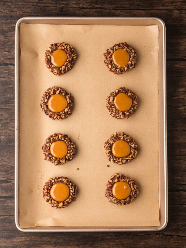 Baked thumbprint cookies filled with smooth caramel on a baking sheet.