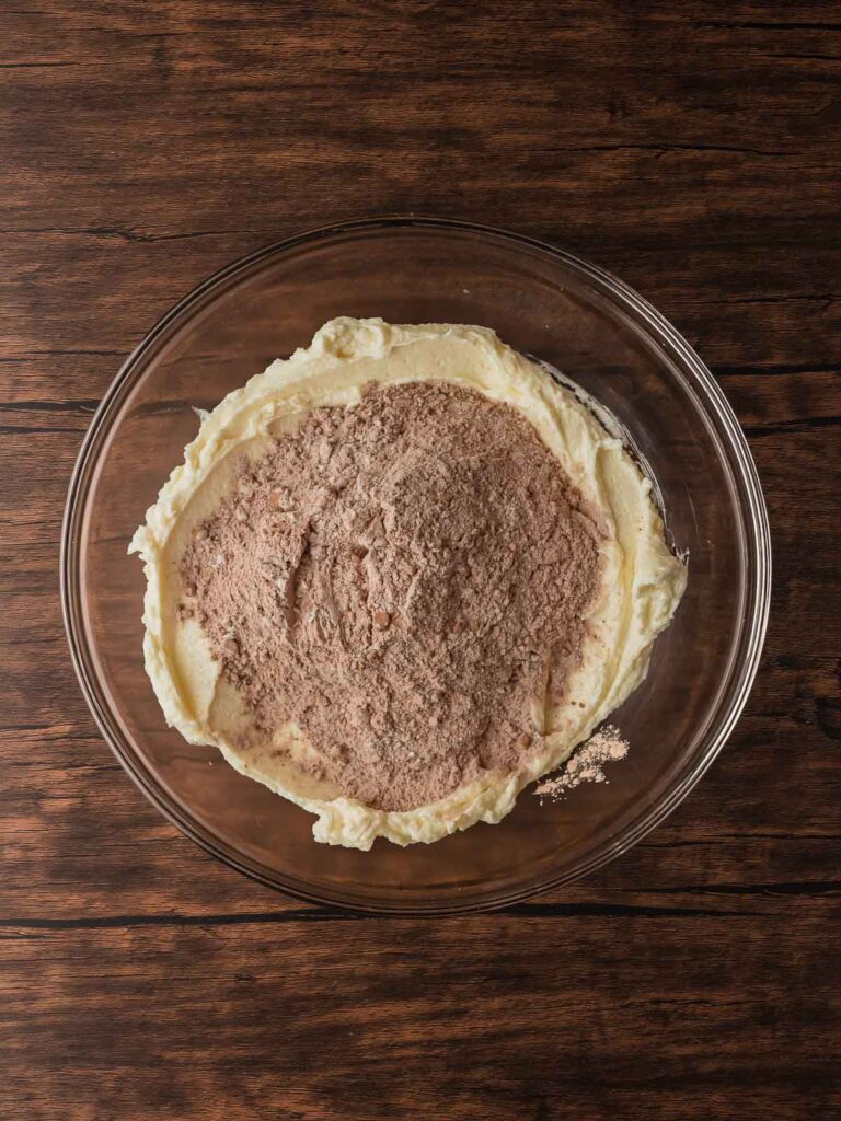Dry ingredients, flour, cocoa powder being added to the wet ingredients, and salt in a glass bowl before mixing.