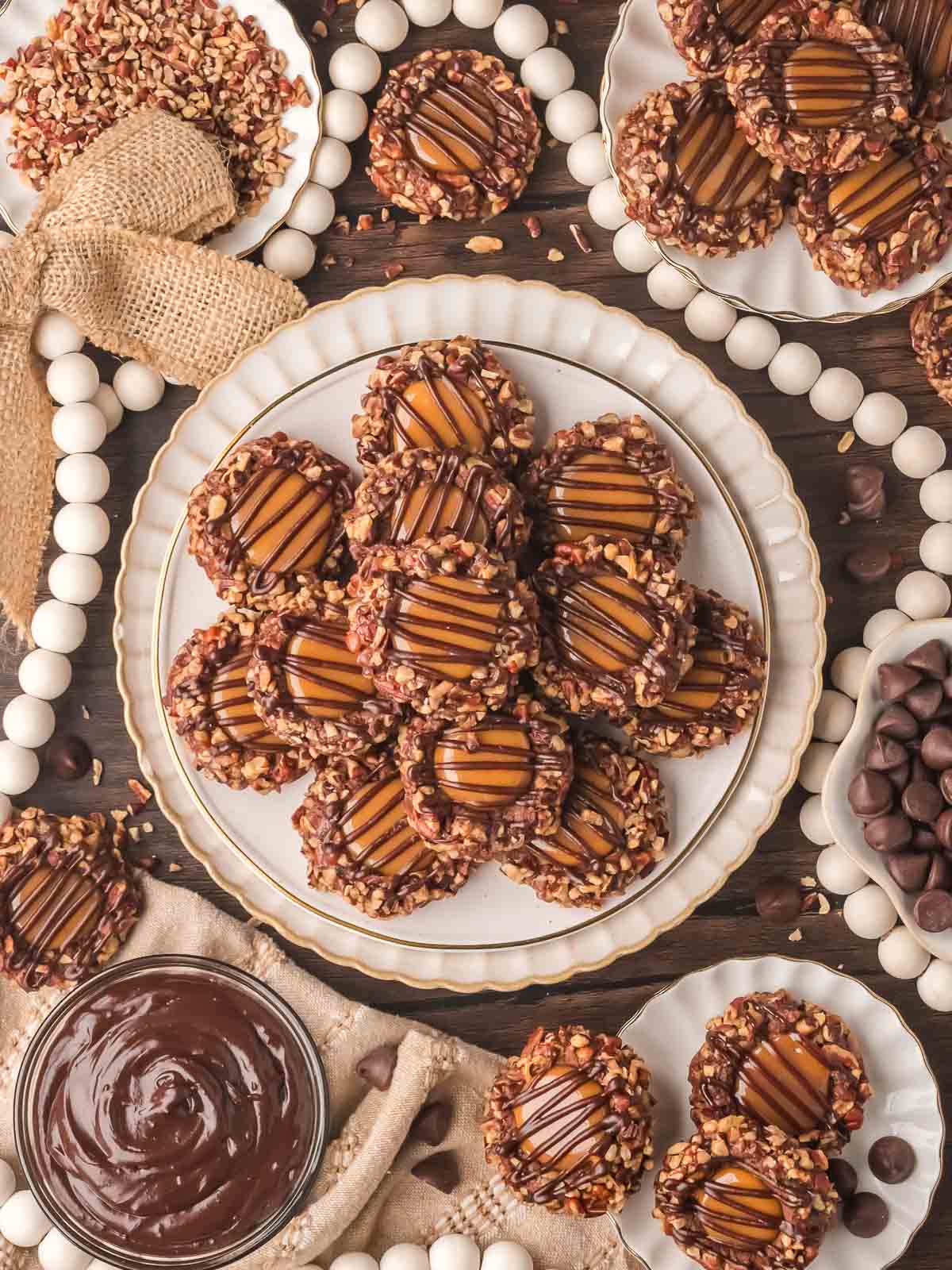 Turtle Thumbprint Cookies arranged on plates with chopped pecans and melted chocolate.