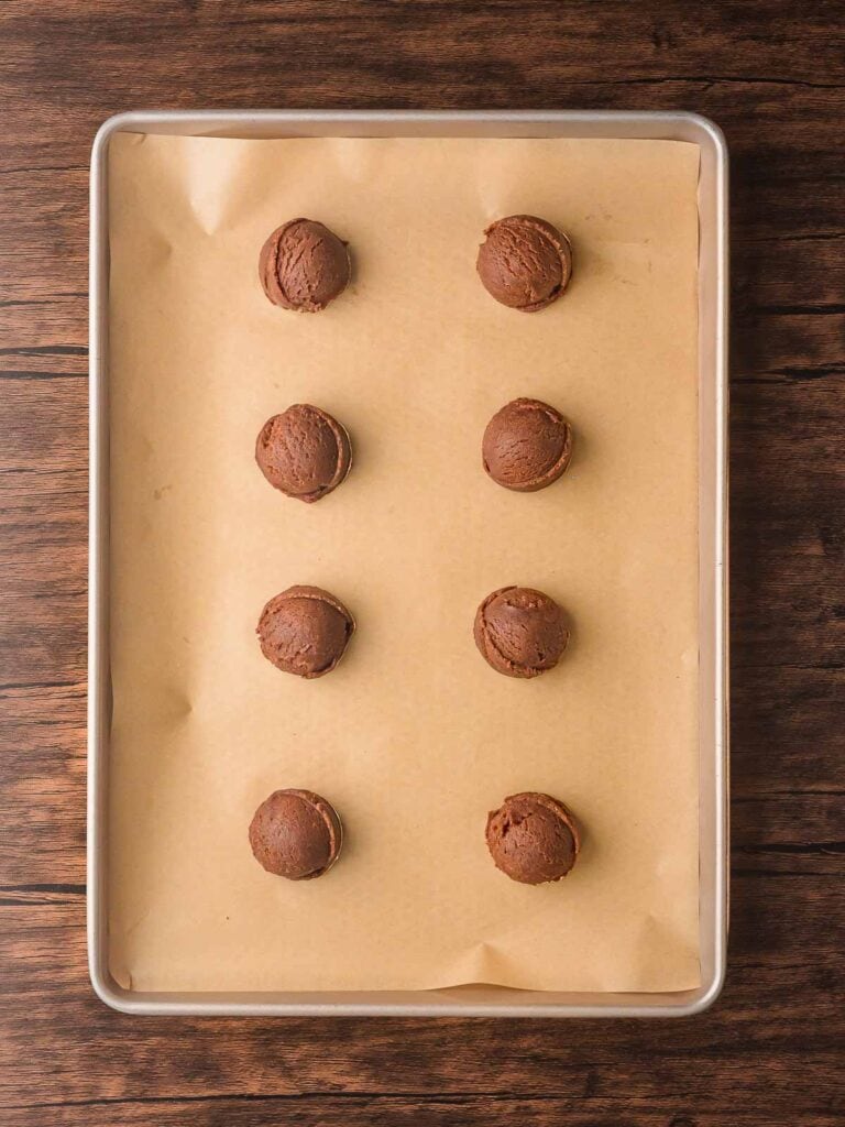 Scooped chocolate cookie dough balls arranged on a parchment-lined baking sheet.