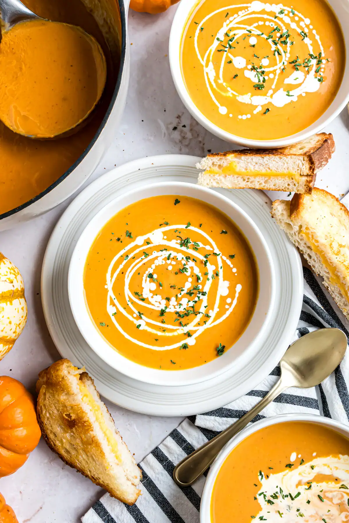 Two bowls of Pumpkin tomato soup with grilled cheese sandwiches on the side.