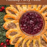 Close-up of a sausage roll wreath around a bowl of cranberry sauce on evergreen branches by Tessie's Table.