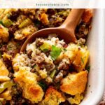 Wooden spoon scooping sourdough stuffing with sausage and celery from a white baking dish by Tessie's Table.