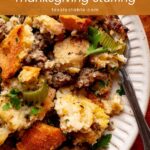 Close-up of sourdough stuffing with sausage, celery and parsley on a white plate with a fork by Tessie's Table.